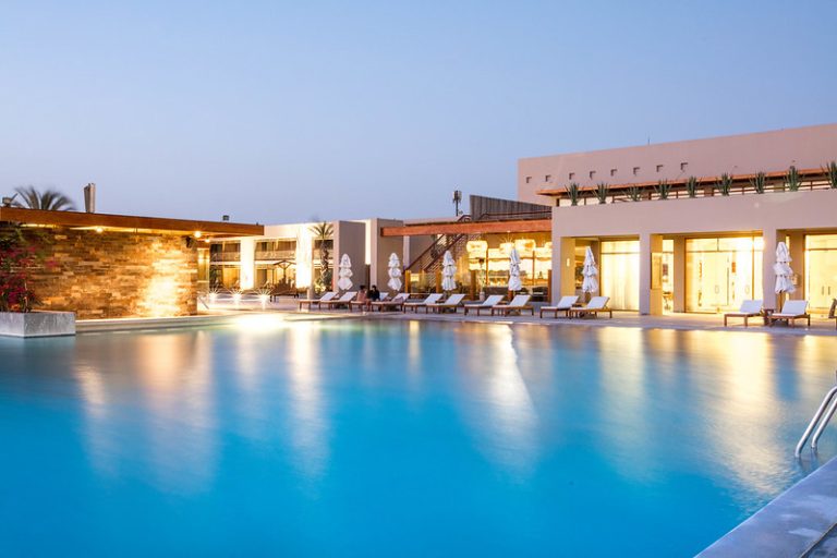 Outdoor pool area of DoubleTree Paracas hotel with lounge chairs and palm trees.