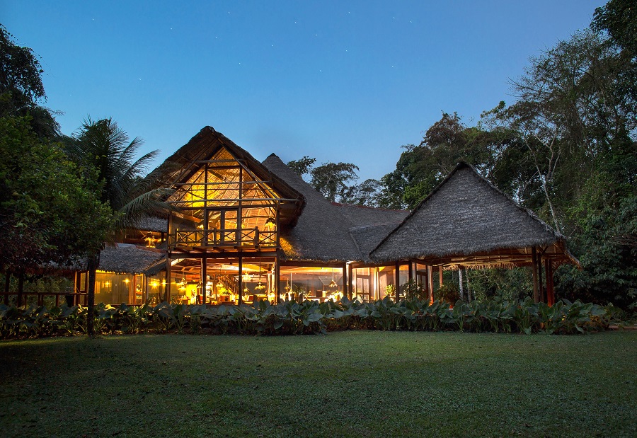 Luxury hotel with lit water features at twilight, set against mountains in the background.