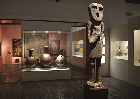 A museum exhibit in Lima featuring ancient pottery, a large stone statue in the foreground, and artifacts displayed in glass cases.