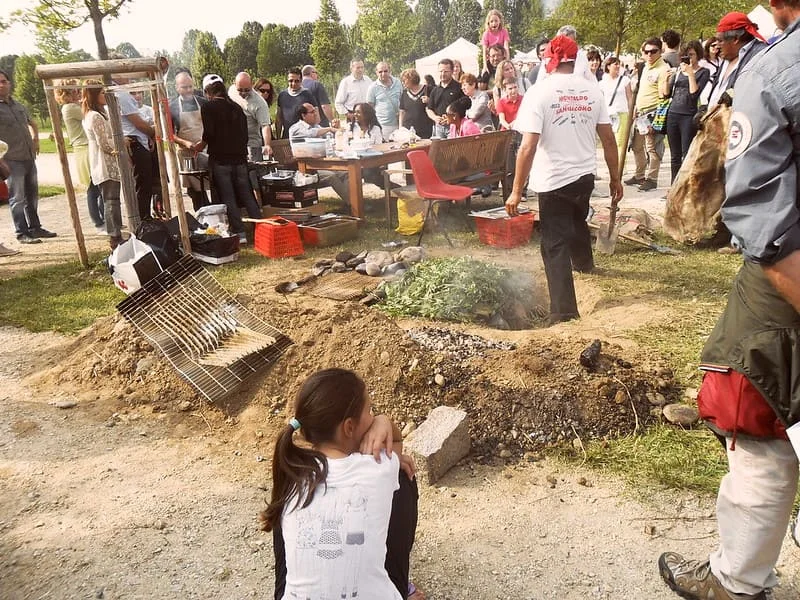 Group of people watching a pachamanca being prepared at an outdoor event.