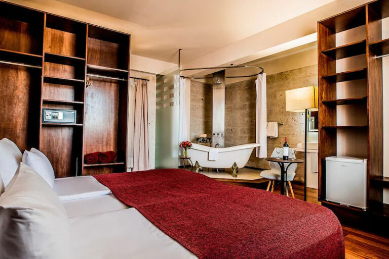 Modern hotel room at Palla Boutique Hotel with large bed, freestanding bathtub, and wooden shelves.