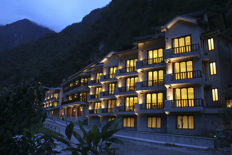 Luxury hotel with lit water features at twilight, set against mountains in the background.
