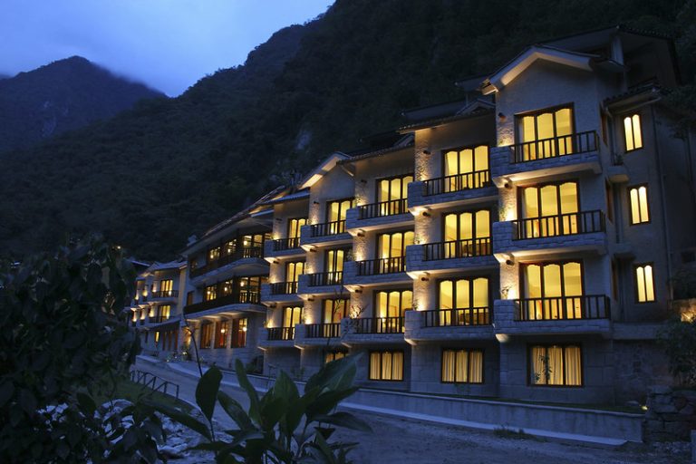 Luxury hotel building illuminated at night, surrounded by mountains.