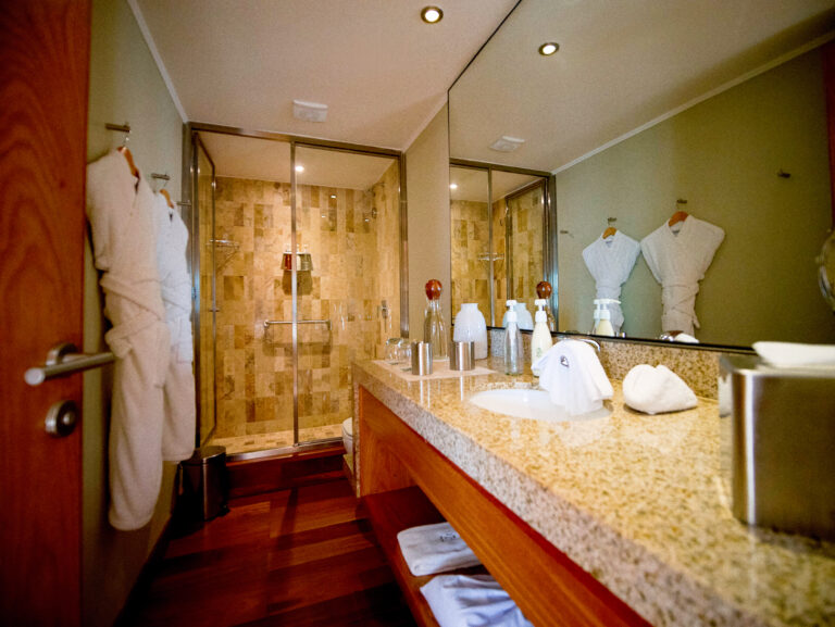 Luxury bathroom aboard an Amazon river cruise in Peru. Elegant design with granite countertops, a glass-enclosed shower, and plush bathrobes for a high-end travel experience.